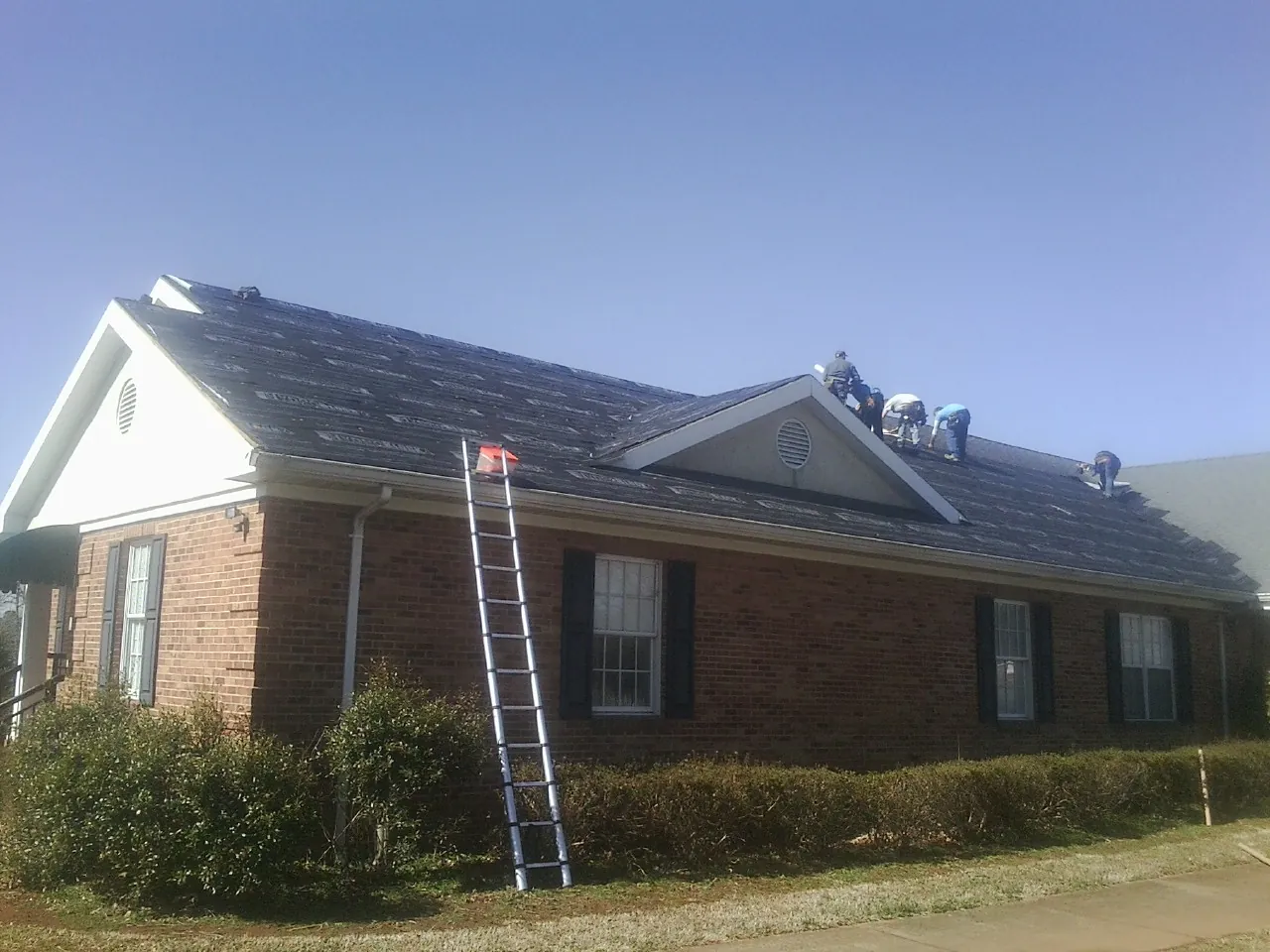Crew tearing shingles off a brick ranch roof with a ladder set — Metal Roof Repair work by our crew in Paradise